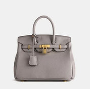 Borsa Birkin grigia in pelle con dettagli dorati, manico superiore e chiusura a lucchetto. Elegante accessorio di lusso per moda femminile.