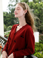 A woman wearing a red knit cardigan with embroidery.