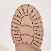 Nahaufnahme der Sohle eines Stiefeletten. Das strukturierte Profildesign ist vor einem einfarbigen Hintergrund zu sehen.