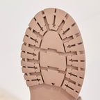 Nahaufnahme der Sohle eines Stiefeletten. Das strukturierte Profildesign ist vor einem einfarbigen Hintergrund zu sehen.